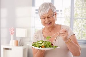 Happy older woman eating a salad by herself