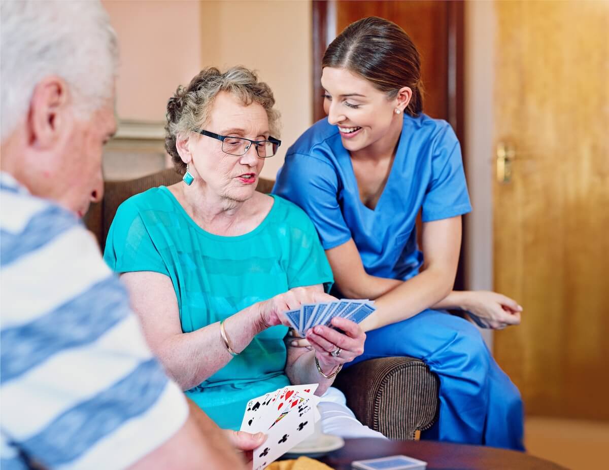 Caregiver with an older woman playing cards.