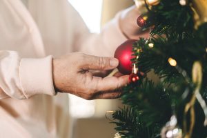 Older adult placing a Christmas sphere on a tree.